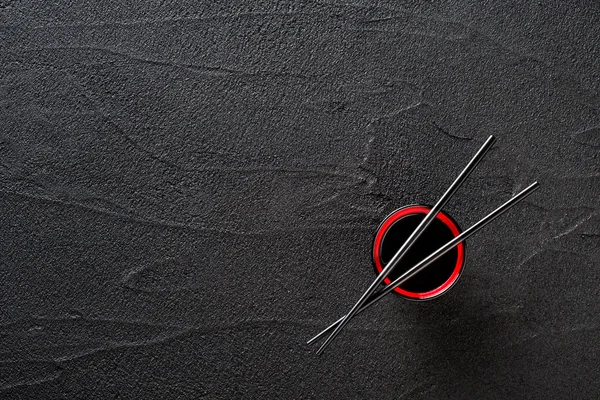 Chopsticks and bowl with soy sauce on black stone background — Stock Photo, Image