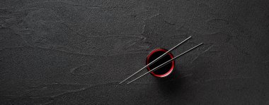 Chopsticks and bowl with soy sauce on black stone background clipart