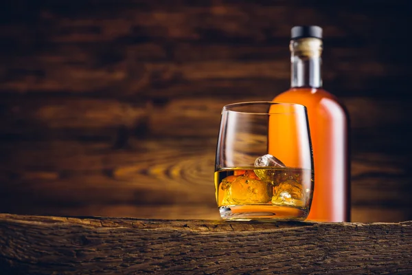 Vidro de uísque e garrafa na velha mesa de madeira — Fotografia de Stock