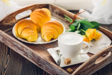 Kahve, kruvasan ve tepsi ahşap bir masa üzerinde çiçekler