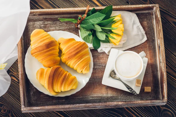 Café, croissant e flores na bandeja em uma mesa de madeira — Fotografia de Stock