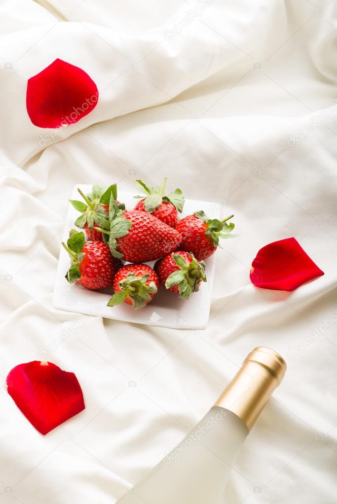 Strawberry, wine and  rose petals on bed