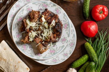 Beyaz bir tabakta kebap, soğan turşusu, koyu bir masada.