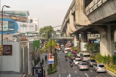 Bangkok, Tayland - 22 Ocak 2025: Kalabalık şehir caddesi, arabalar, taksiler, motosikletler ve beton tren raylarının altında otobüsler. Ağır trafik ve çeşitli araçlarla şehir ulaşımı sahnesi.