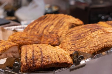 Gıda tezgahında satılan domuz eti göbeğinin yakın plan görüntüsünde, derisi altın ve çıtır olana kadar kızartılmış veya kızartılmış kalın bir domuz eti tabakası yer alıyor..