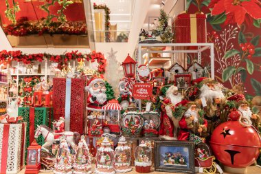 Renkli bir Noel vitrininde Noel Baba heykelcikleri, paketlenmiş hediyeler, süslü süsler ve canlı bir tatil dekoru sergileniyor.