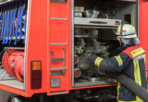 Brandweerman omvat een brandslang aan de noodsituatie voertuig. — Stockfoto