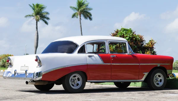 HAVANA, CUBA - JUNHO 17, 2015: Cuba vermelho branco americano clássico carro estacionado sob as palmas das mãos no local de estacionamento — Fotografia de Stock