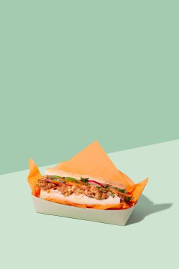 Vietnamese Banh Mi sandwich with roasted cauliflower and pickled veggie in takeaway packaging box on green background with copy space.Restaurant food delivery concept clipart