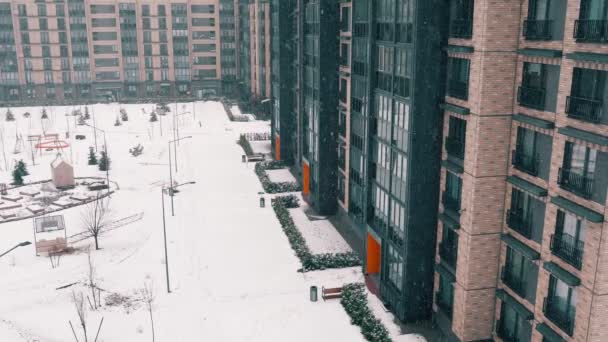 Paesaggio urbano inverno, vista di caduta fiocchi di neve e cumuli di neve. Facciata interna del condominio si affaccia su un cortile ben arredato con design paesaggistico e piccole forme architettoniche. — Video Stock