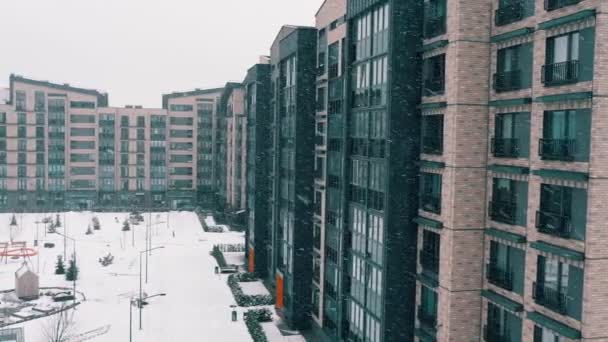 Peisaj de iarnă cu clădire de apartamente. Fațada casei cu mai multe etaje, Vedere de fulgi de zăpadă care cad și derivă în curte. Arhitectură casă urbană, agenție imobiliară în conceptul modern, nou, elegant al orașului . — Videoclip de stoc
