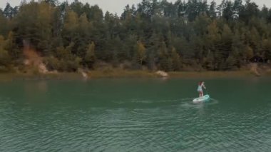 Bikinili genç kızın havadan görünüşü yemek masası küreğinde, su aktivitelerinde, macera denizinde, spor eğlencelerinde yükseliyor. Okyanus dalgalarında sörf yapan kadın, plajlı yaz manzarası, yeşil ağaçlar ve gökyüzü