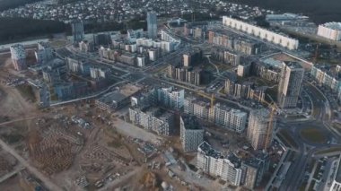 Şehir caddesinin üst manzarasında inşaat yeni çeyrekliği. Bitmemiş evleri, inşaat işleri, kule vinçleri ve kumları olan bir inşaat alanı. Yolları ve trafik arabaları olan şehir manzarası