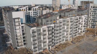 İnşaat alanının havadan görünüşü ve tamamlanmamış apartman bloklarının ön cephesi. Çalışma süreci modern bir apartman dairesi. Şehir caddesinde çatısı, penceresi ve balkonu olan bir ev.