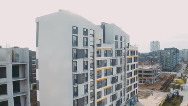 Construction site, building work process modern an apartment panel house on town street. Unfinished structure city block of flats. Aerial view of facade with windows, pitched roofs and road — Stock Video