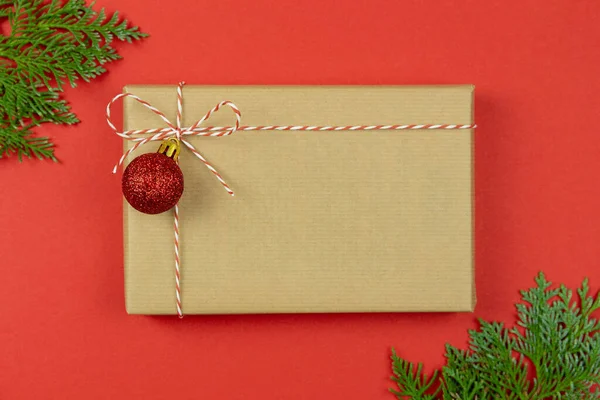 Christmas gift box wrapped in kraft paper with thuja branches and decoration on red background. Holiday card concept. Top view. Copy space. Flat Lay. Mockup. — Stock Photo, Image