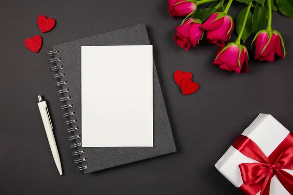 Tarjeta de felicitación y caja de regalo con cinta roja, corazones, rosas sobre fondo oscuro. Plano concepto laico de San Valentín, aniversario, el día de la madre y el saludo de cumpleaños. Vista superior. Copiar espacio. Burla.. — Foto de Stock