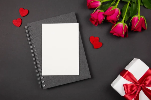 Tarjeta de felicitación y caja de regalo con cinta roja, corazones, rosas sobre fondo oscuro. Plano concepto laico de San Valentín, aniversario, el día de la madre y el saludo de cumpleaños. Vista superior. Copiar espacio. Burla.. — Foto de Stock