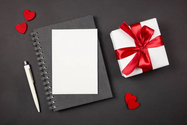 Tarjeta de felicitación y caja de regalo con cinta roja y corazones sobre fondo oscuro. Plano concepto laico de San Valentín, aniversario, el día de la madre y el saludo de cumpleaños. Vista superior. Copiar espacio. Burla.. — Foto de Stock