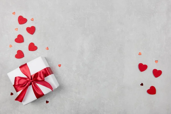 Fondo de San Valentín con regalo y corazones rojos confeti sobre fondo de hormigón claro. Día de San Valentín o madre, cumpleaños, concepto de vacaciones. Plano, vista superior, espacio para copiar. — Foto de Stock