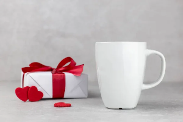 Taza blanca en blanco maqueta con caja de regalo y corazones rojos, fondo de piedra de hormigón ligero. San Valentín, madres, composición del día de las mujeres. Vista lateral. Copiar espacio. — Foto de Stock