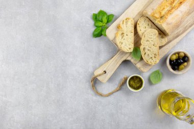 Bitkilerle birlikte taze İtalyan ciabatta ekmeği, zeytinyağı, siyah ve yeşil zeytin, fesleğen yaprağı ve açık beton zemin üzerine pesto sosu. Üst Manzara. Boşluğu kopyala.