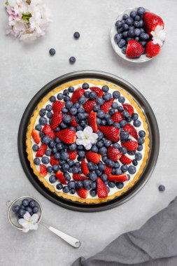 Açık gri arka planda krem şanti ve mascarpone ile lezzetli yaban mersinli ve çilekli tart. Üst görünüm. 