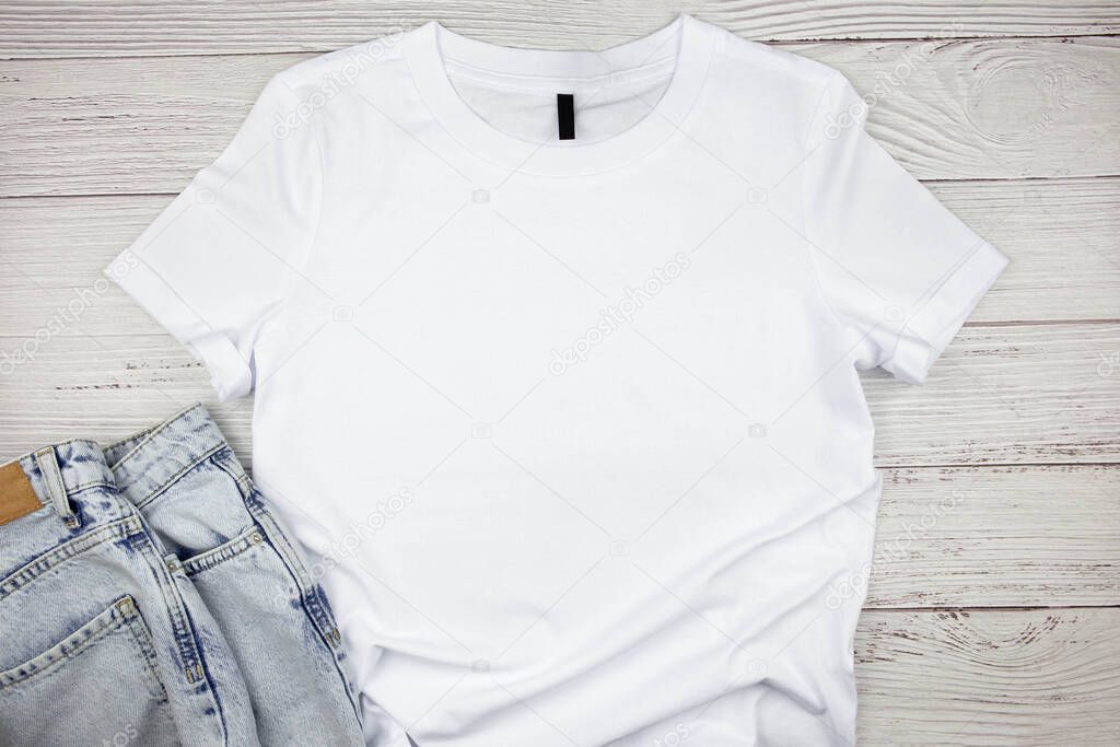 White womens cotton Tshirt mockup with blue jeans pants on wooden background. Design t shirt template, print presentation mock up. Top view flat lay. 