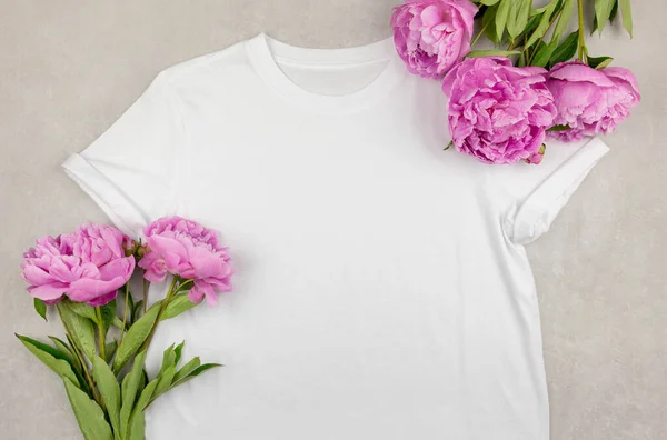Witte womens katoenen t-shirt mockup met roze pioenachtige bloemen op grijze betonnen achtergrond. Design t-shirt template, print presentatie mock up. Bovenaanzicht vlak lay. — Stockfoto