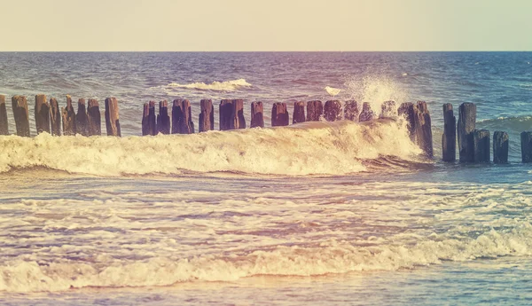 Retro stylized picture of wave crashing against wooden posts — Stock Photo, Image