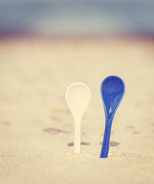 Vintage stylized two porcelain spoons stuck in sand. — Stock Photo, Image