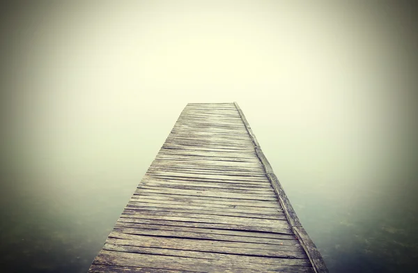 Retro gefiltertes Bild eines alten Holzstegs im dichten Nebel. — Stockfoto