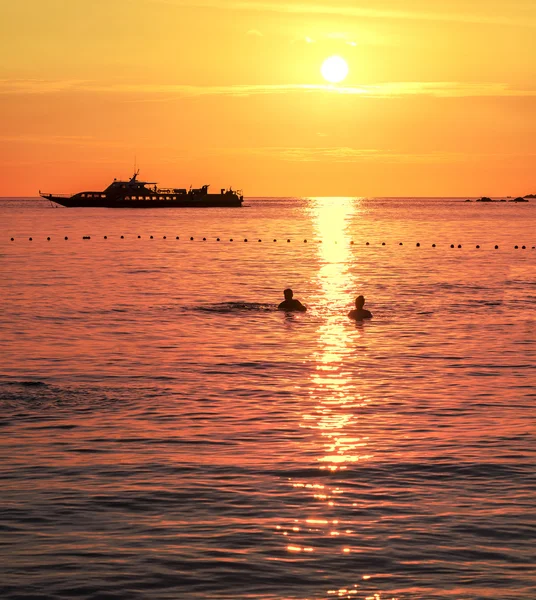 Silhouetten eines schwimmenden Paares und Schiffes bei Sonnenuntergang. — Stockfoto