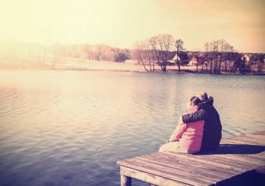 Retro filtered photo of a couple sitting on pier. clipart
