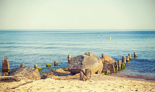Retro toned rocks and wooden posts on the beach. — Stockfoto