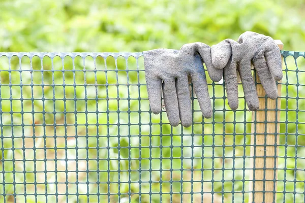 Dirty garden gloves on a plastic fence.