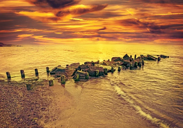 Vintage tonificado pôr do sol dramático sobre praia e cais rochoso . — Fotografia de Stock