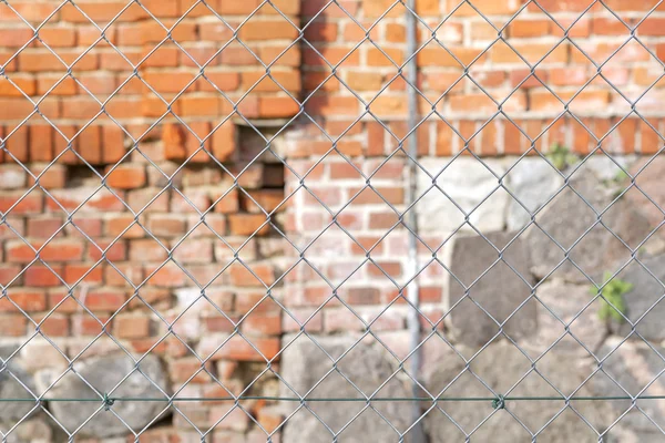 Проволочный забор перед кирпичной стеной, мелкая глубина резкости — стоковое фото