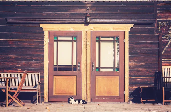 Photo tonique vintage d'un chat devant une maison en bois — Photo