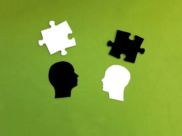 Two silhouettes of the head, two pieces of puzzles in white and black on a green background.  Dialogue, negotiations, decision-making.