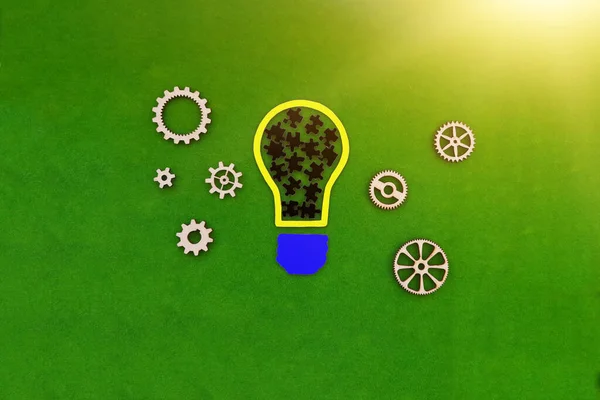 Puzzles in black inside a light bulb, wooden gears on a green background. Business projects, effective teamwork.