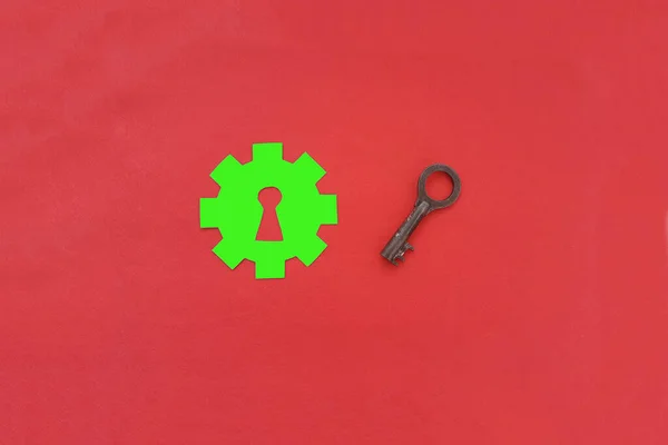 A green cog with a keyhole, a key to a lock made of old iron on a red background.