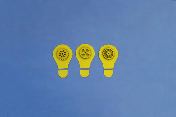Three electric light bulbs, yellow wooden gears on a blue background. The concept of party membership, a common idea. Joint business plan.