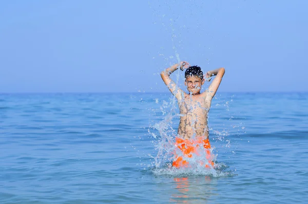 Tonårspojke leker med vattnet i havet. — Stockfoto