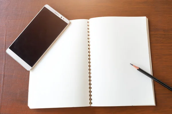 Carnet vierge avec crayon et smartphone sur fond de table en bois — Photo