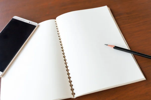 Ahşap masa backg kalem ve smartphone ile boş Not kitap — Stok fotoğraf