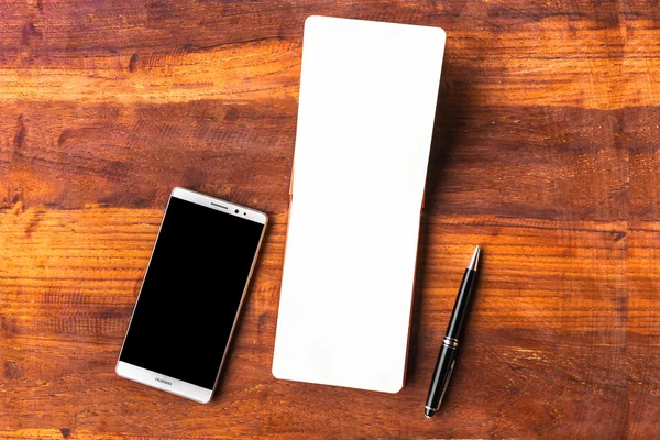 Papel en blanco con bolígrafo y smartphone sobre mesa de madera — Foto de Stock