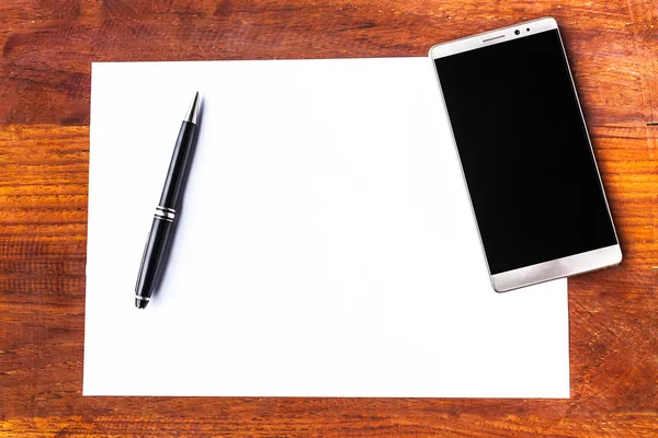 Boş kağıt kalem ve ahşap masa üstünde smartphone ile