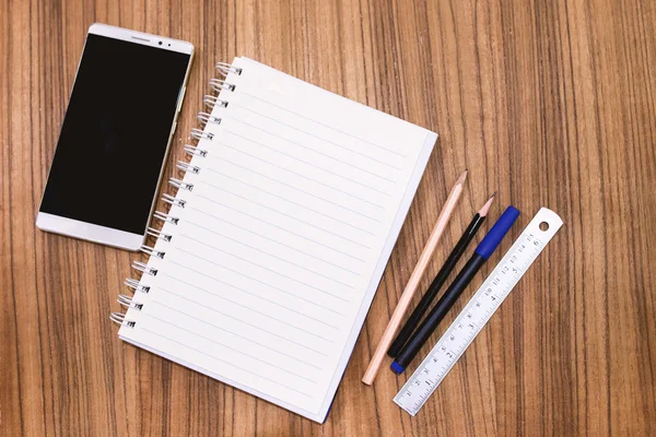 Ahşap masa con üzerinde kalem kalem ve smartphone ile boş not defteri — Stok fotoğraf