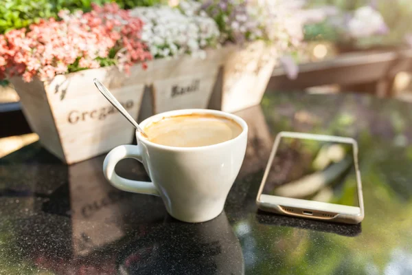 Digital smartphone and cup of coffee on desk with vintage flower